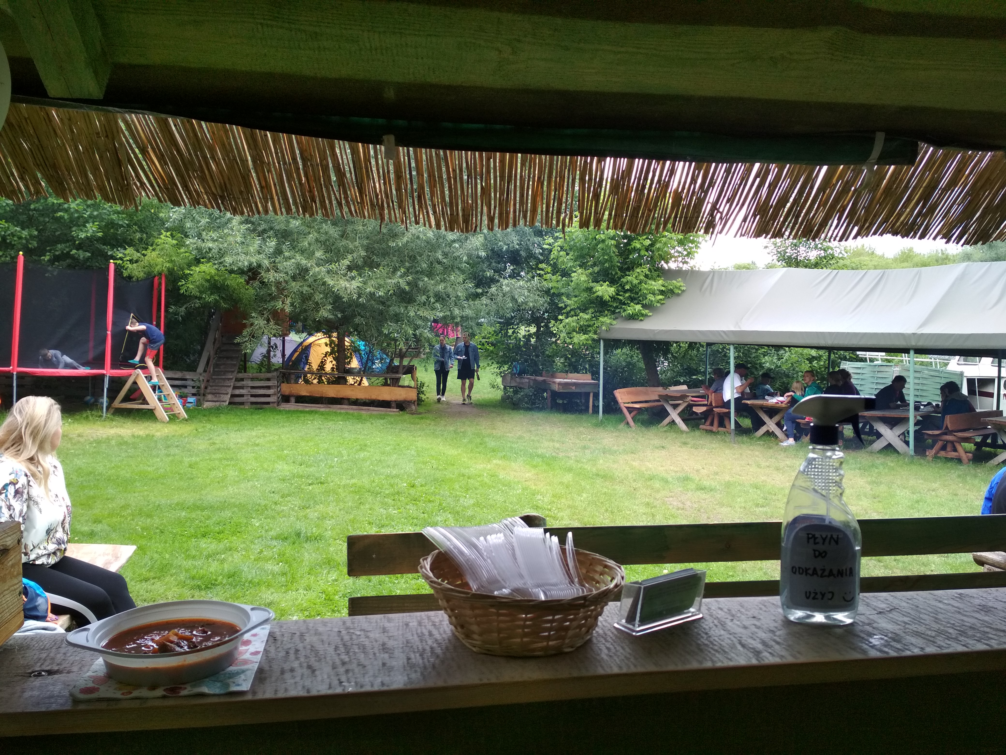 Widok z przystaniowej kuchni na odpoczywające na polu namiotowym osoby.