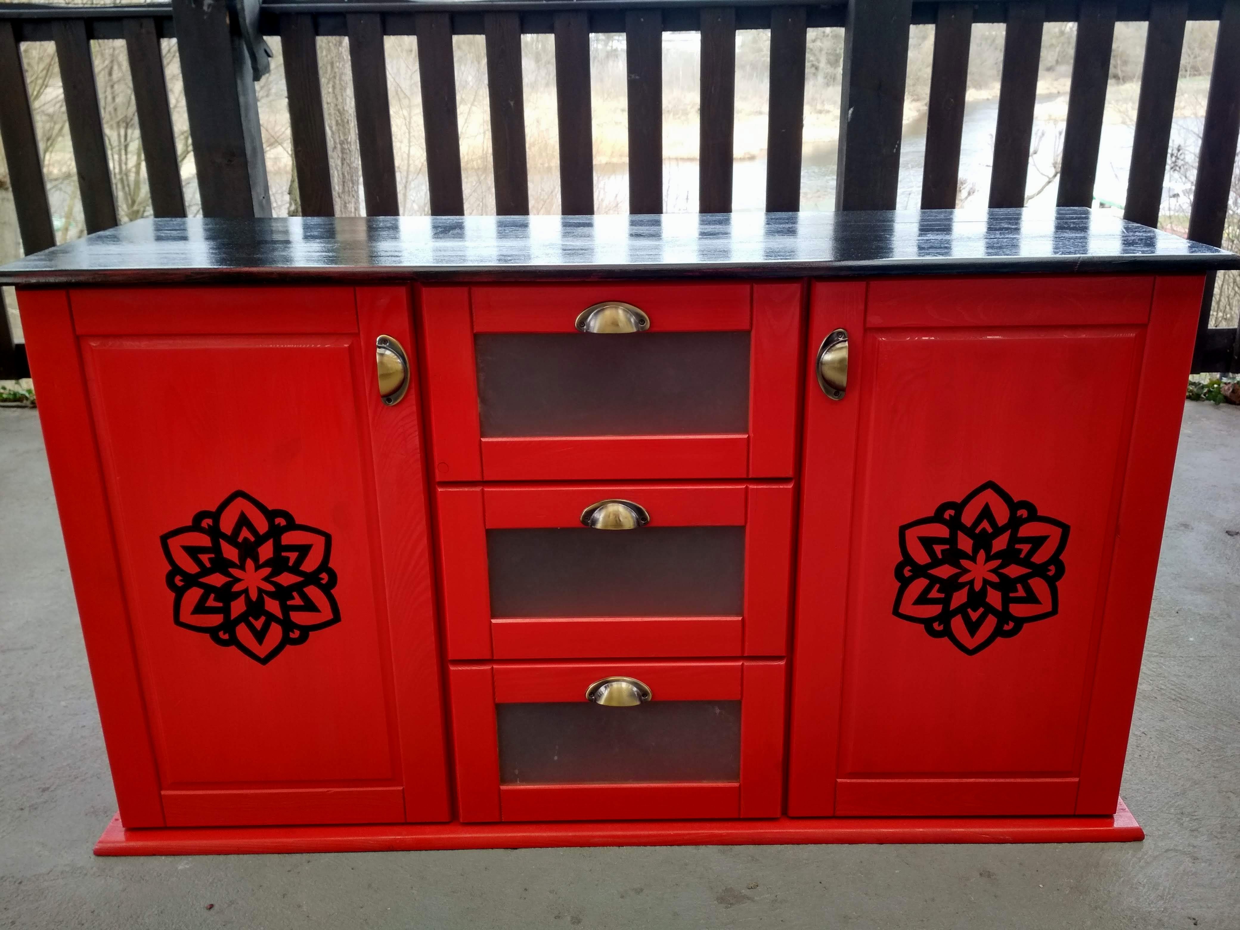 Czerwona komoda z czarnym blatem i czarnymi dekorami ręcznie malowanymi na drzwiczkach. 3 pojemne szuflady.
