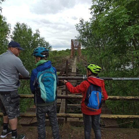 Na zdjęciu widoczne trzy osoby. Mężczyzna i dwóch chłopców. Stoją przy barierach przed mostem kolejowym.