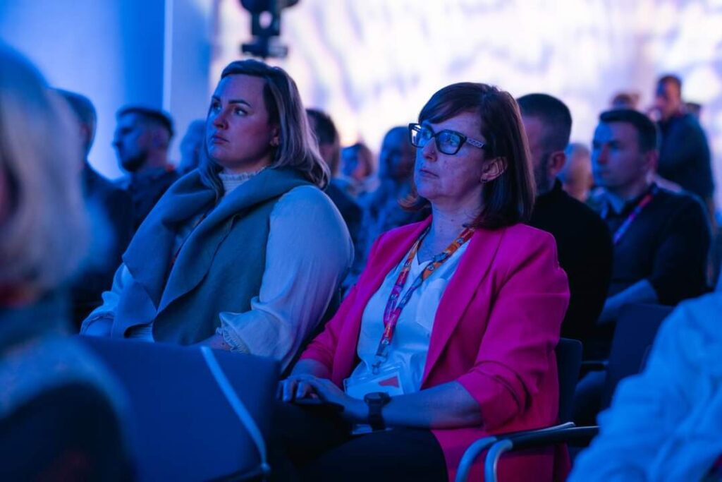 Dwie kobiety uczestniczą w konferencji słuchając prelekcji, wokół inni uczestnicy. Kongres Firm Oborniki 2024