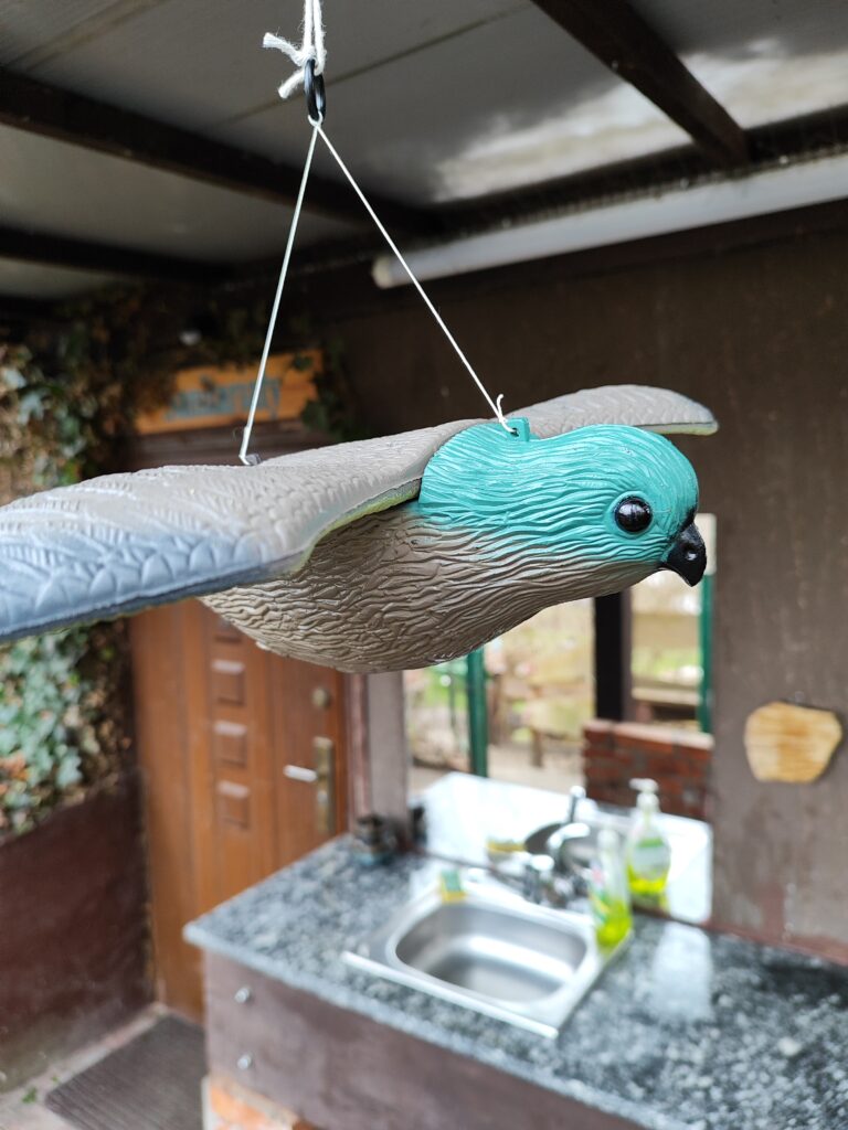 plastikowy szaro niebieski ptak- pustułka zawieszona by odstraszać ptaki i by nie uderzały o lustra